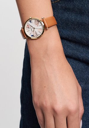 Runde Uhr mit weißem Zifferblatt mit Blumenmuster, goldenem Gehäuse und hellbraunem Lederarmband, getragen am Handgelenk.