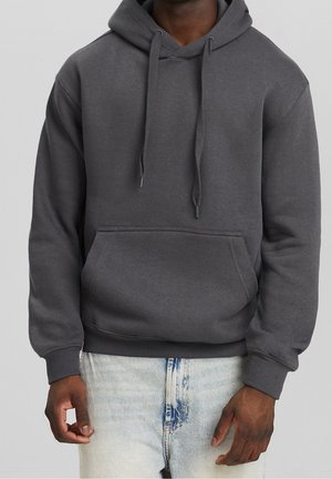 Sweatshirt à capuche gris foncé avec une poche avant, des cords de serrage, des poignets et un ourlet côtelés, porté sur un jean léger bleu déchiré.
