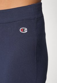 Marineblauwe joggingsbroek met een elastische tailleband, voorzien van een geborduurd rood en wit logo aan de linkerkant, gladde stofstructuur.