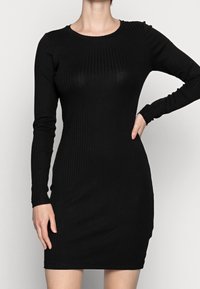 Svart ribbad långärmad klänning med en figurnära silhuett, rund halsringning och textilstruktur. Längd till mitten av låret med subtil stretch.