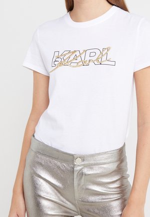 Witte katoenen T-shirt met het 'KARL' logo in zwarte omranding en gouden versiering. Model draagt het met metallic zilveren broeken.