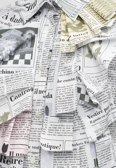 Κοντινή εικόνα διπλωμένου υφάσματος τυπωμένου με διάφορα κείμενα και εικόνες εφημερίδας σε μαύρο και άσπρο με κάποιες πράσινες λεπτομέρειες.