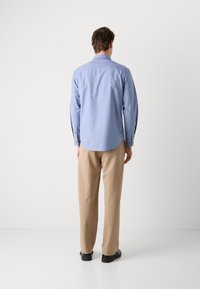 Camisa azul de mangas compridas com botões nos punhos, bainha curva, combinada com calças bege e sapatos pretos. Design simples, tecido leve.