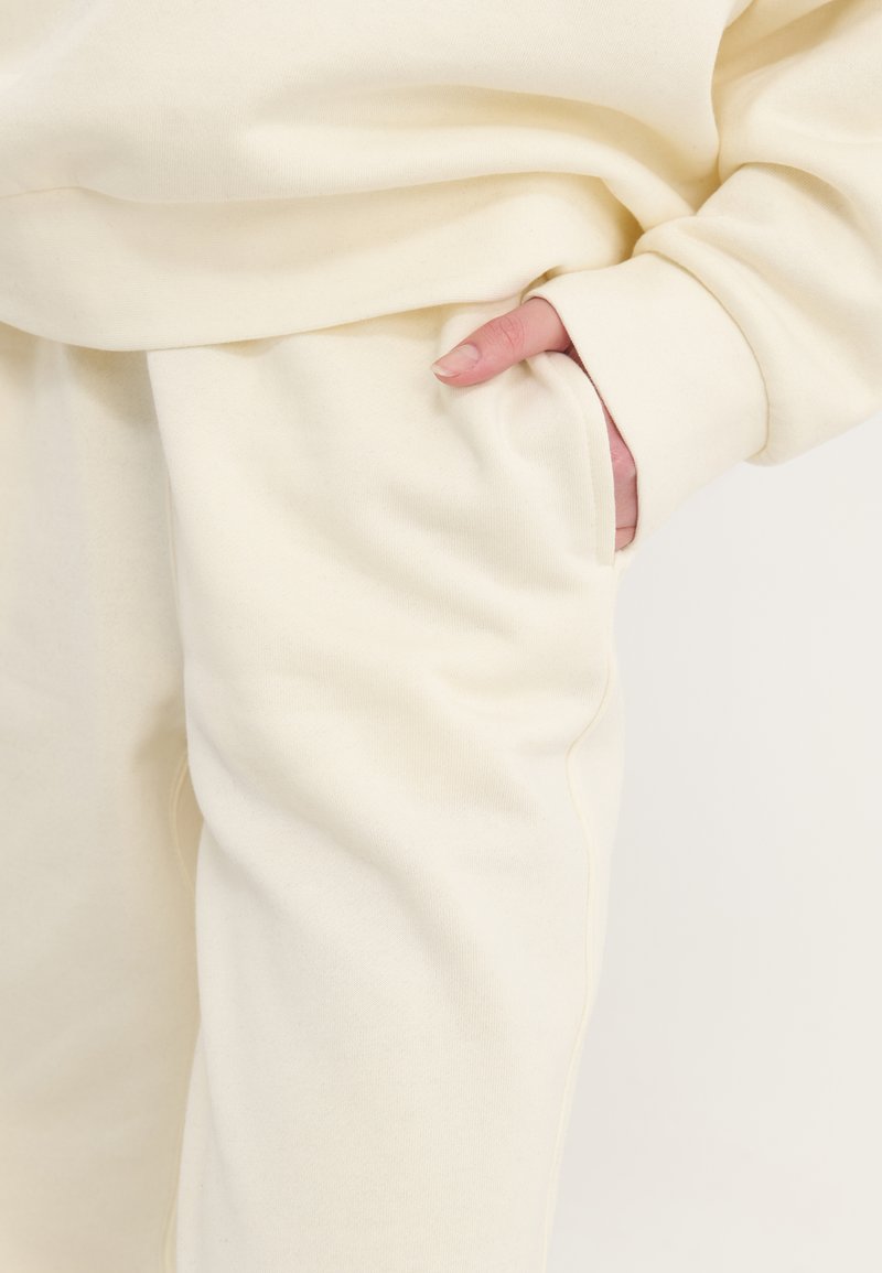 Set di abbigliamento comodo di colore crema con una texture morbida, vestibilità rilassata e dettaglio con tasca laterale sui pantaloni.