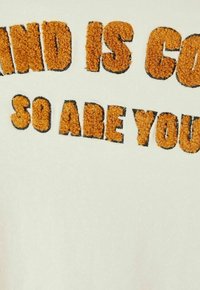 Off-white sweatshirt featuring fuzzy, orange lettering stating, "WINTER IS COMING SO ARE YOU." The text has a textured, plush appearance.