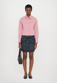 Rosa skjorte med knapper, mørk denimskjørt, svarte leiligheter og en liten svart håndveske. Rett-snitt design, klassisk krage og minimalistisk stil.