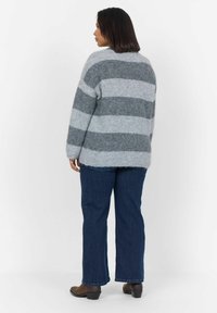 Pull en gris rayé fabriqué dans un matériau doux, avec de larges rayures horizontales et une coupe décontractée. Associé à un jean bleu foncé et des bottes marron.