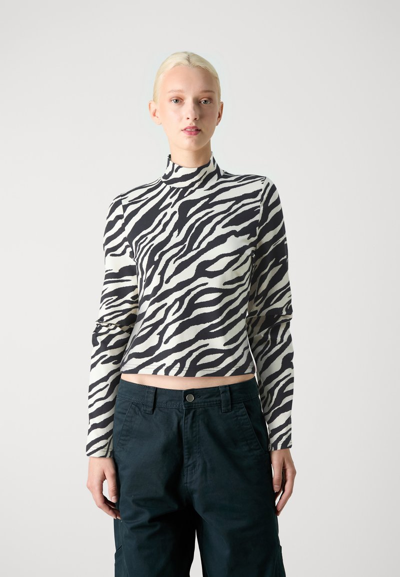 Top recortado a rayas blanco y negro con cuello alto y mangas largas, combinado con pantalones de tiro oscuro verde, mostrando una textura de tela suave.