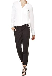 Chemise blanche à manches longues avec une poche poitrine, associée à un pantalon noir fuselé avec des accents cloutés et des poignets retournés. Escarpins noirs à lanières.