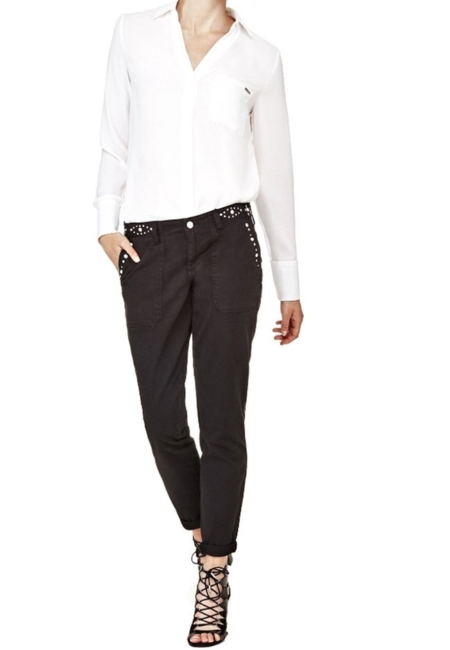 Chemise blanche à manches longues avec une poche poitrine, associée à un pantalon noir fuselé avec des accents cloutés et des poignets retournés. Escarpins noirs à lanières.