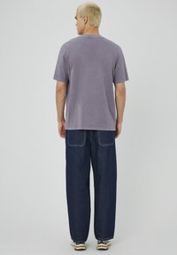 T-shirt gris à manches courtes et jeans en denim bleu foncé à coupe décontractée. T-shirt avec col rond ; les jeans comportent deux poches arrière et des surpiqûres contrastées.