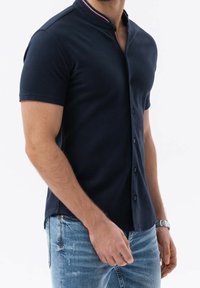 Polo de manga corta en color marino con collar abotonado, que presenta una delgada franja roja y blanca a lo largo del escote y un tejido texturizado.
