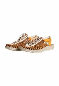 Sandales tressées beige avec une semelle légère beige, dotées de lacets élastiques, d'une sangle à l'arrière et d'un design texturé.