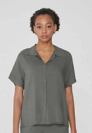 Camisa de manga corta con cuello en tela verde oscuro de textura suave, que cuenta con cierre de botones en la parte delantera y un corte relajado. Los botones son de un tono a juego.