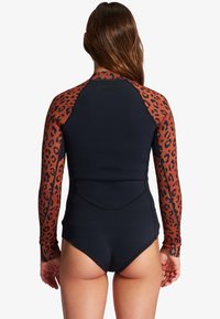 Une combinaison de plongée à manches longues avec un corps noir et des manches à motif léopard orange, fabriquée dans un matériau extensible avec des coutures plates pour le confort.