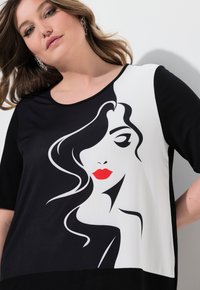 Černobílý krátký rukáv top s grafickým designem ženské tváře s červenými rty a splývavými vlasy, vyrobený z měkké tkaniny.