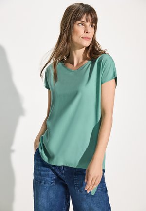 Haut vert menthe à manches courtes avec un col rond, texture lisse et coupe décontractée, associé à un pantalon en denim bleu foncé avec poches.