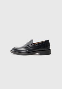 Mocassins en cuir noir avec un design cousu, bout rond, talon bas empilé et détail de logo estampé sur le côté. Texture lisse.
