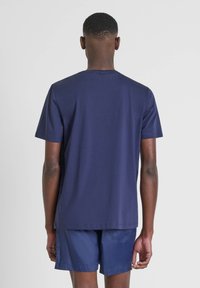 T-shirt a maniche corte blu navy realizzato in tessuto morbido, con scollatura rotonda e orlo dritto. Indossato con pantaloni corti abbinati.
