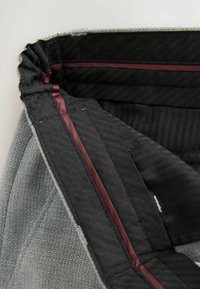 Tessuto grigio con motivo a rilievo, interno nero a contrasto, presenta una fodera e zip bordeaux lungo il bordo.