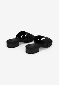 Sandalias de tacón negras con un upper texturizado, que presentan tiras anchas cruzadas y un tacón cuadrado. Plantilla suave y detalles mínimos.