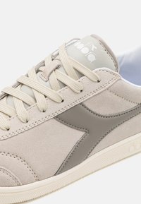 Sneakers beige in suede con accenti grigi, pannelli laterali testurizzati, lacci piatti beige e suola in gomma bianca. Logo stampato sulla linguetta.