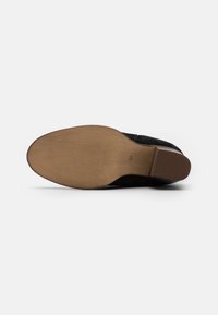 Suela de zapato de ante negro con una suela de goma marrón. Patrón de agarre texturizado y ligero tacón. Tamaño 37 claramente marcado cerca del tacón.