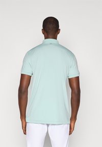 Polo azul claro feito de tecido suave, com colarinho, mangas curtas e um logótipo discreto nas costas, perto do decote.