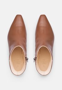 Bottines en cuir marron avec un bout pointu, dotées d'une fermeture éclair sur le côté et d'une texture lisse. L'intérieur est doublé d'un coloris clair avec une marque.