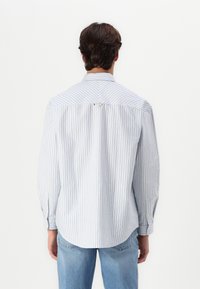 Camisa de botones a rayas en tejido de color azul claro y blanco, con mangas largas, detalle de pliegue en la parte posterior y un dobladillo curvado.