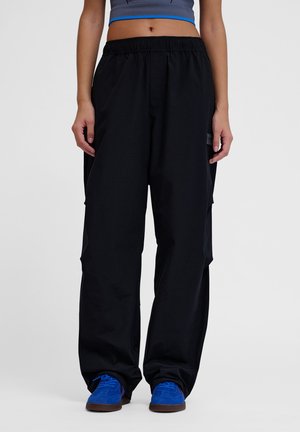 Schwarze Cargo-Hosen mit entspannter Passform, elastischem Bund und Seitentaschen. Getragen mit blauen Wildlederschuhen. Glatte Stoffstruktur.