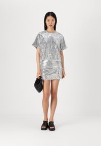 Abito argento con paillettes, maniche corte, orlo con frange, abbinato a una borsa nera e sandali neri. Design minimalista, texture lucida.