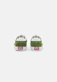 Zelené semišové tenisky s bílými akcenty, tradiční nízký design a červené logo Vans na patě. Hladký povrch a čisté linie.