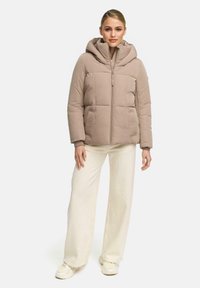Beige puffer jacket with a hood, featuring a zippered front, two side pockets, and a quilted texture. Paired with white wide-leg pants.