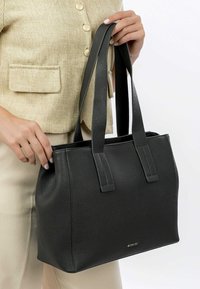 Sort læder tote taske med en tekstureret overflade, to robuste håndtag og en struktureret form. Minimalistisk design med en diskret logo detalje.