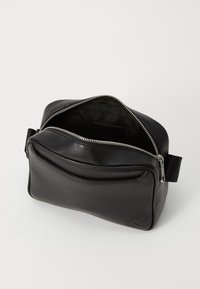 Black leather zippered pouch with front pocket, partially open showing black fabric interior, and embossed "cK" logo on lower right corner.