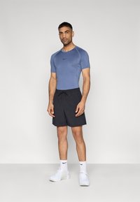 Αθλητική στολή ανδρών που περιλαμβάνει εφαρμοστό μπλε πουκάμισο, μαύρο σορτς με κορδόνι και λευκά αθλητικά παπούτσια με μαύρες λεπτομέρειες.