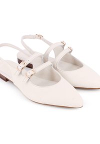 Zapatos slingback blancos de cuero, con punta afilada, lados recortados y dos correas ajustables con detalles en dorado.