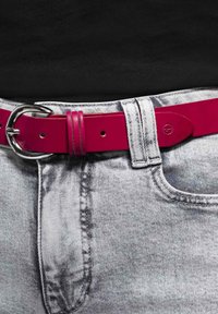 Rosa Lederpass mit einer silbernen Metallschnalle, getragen über hellgrauen Jeans. Der Gürtel hat gestanzte Löcher und eine ordentliche Naht.