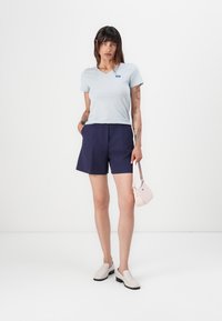 Ljusblå v-ringad t-shirt, marinblå skräddarsydda shorts, krämfärgade slip-on skor och en rosa handväska. Släta texturer och enkel design.