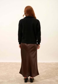 Zwarte gebreide trui met lange mouwen, gecombineerd met een vloeiende bruine satijnen maxi-rok. De rok heeft een soepele textuur en een subtiele glans.