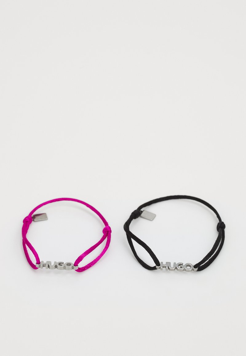 Deux bracelets ajustables : l'un en rose vif et l'autre en noir, tous deux ornés d'un logo "HUGO" en ton argent et d'un design minimaliste.