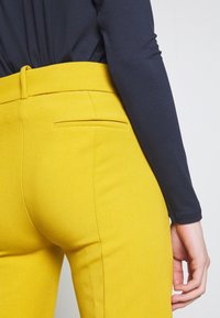Geel op maat gemaakte broeken met een gladde textuur en slim fit, met een achterzak en een gedeeltelijk zichtbare contrasterende marineblauwe top.