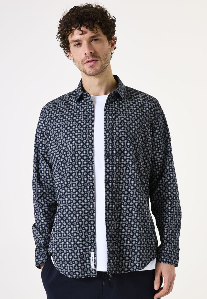 Camisa de botones en azul marino oscuro con un patrón geométrico blanco, con cuello y mangas largas. Hecha de tela de algodón ligera.