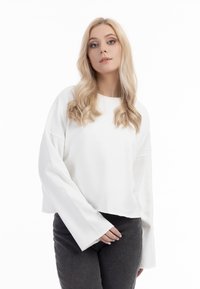 Felpa bianca a maniche lunghe, corta, realizzata in un materiale morbido. Abbinata a pantaloni fitted grigio scuro. Linee semplici e pulite.