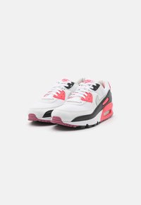 Sapatilhas Nike Air Max 90 com um upper branco, detalhes em preto, pormenores em rosa choque e uma unidade de amortecimento visível na sola.