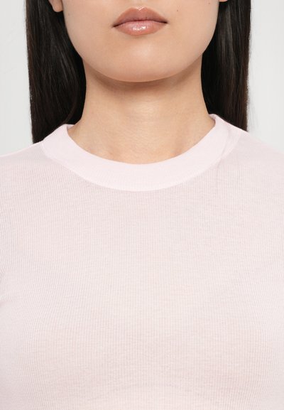 Top ribbed de culoare roz deschis, cu decolteu rotund, având o textură moale și un design mulat, prezentat pe un fundal simplu.