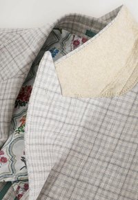 Helles graues Blazerjackett mit Karomuster, ausgestattet mit einem weichen Wollkragen und einem floral gemusterten Innenfutter. Maßgeschneiderte Passform mit präzisen Nähten.