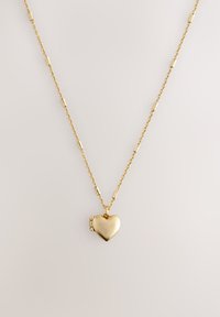 Gold chain necklace featuring a polished heart-shaped pendant. The chain has an alternating design with small cylindrical accents.
