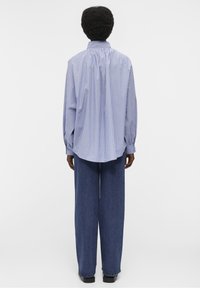 Camicia a righe blu chiaro e bianca con bottoni, vestibilità comoda, maniche lunghe e orlo arrotondato, abbinata a pantaloni di jeans blu a gamba larga.